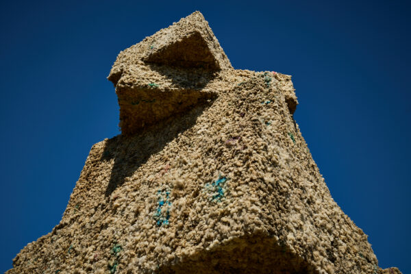 Low-angle view of large stacked oblong shapes forming the wool arch sculpture, showing its textured wool surface against a clear blue sky.