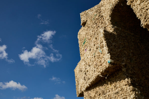 Close-up angled view of the wool arch sculpture, showing its textured wool surface and stacked geometric forms against a deep blue sky with scattered clouds.