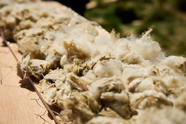 Detailed close-up of raw wool fibres packed against wooden panels and held in place by chicken wire mesh, showing the construction technique used in the wool arch sculpture.